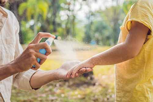 Person applying mosquito spray to child